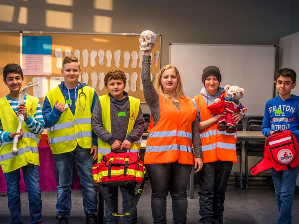 Jugendliche in Warnwesten des Schulsanitätsdienstes stehen mit ihrer Ausrüstung an einem Tisch.